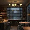 A dimly lit cafe interior with a large window showing a rainy street scene. Produktbild-Vorschau
