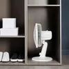 A white desk fan is placed inside a wooden shelf unit next to two white boxes and two pairs of shoes. Náhľad obrázku produktu