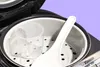 Close-up view of the inside of a rice cooker with a measuring cup and a rice paddle. Produktbild-Vorschau