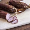 Three sausages are placed on a wooden cutting board, with one sausage sliced into pieces. Produktbild-Vorschau