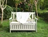 A wooden garden bench with a white blanket and books on it, set in a lush garden. Anteprima dell’immagine prodotto