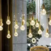 A collection of hanging pendant lights with clear, textured glass bulbs and gold fixtures, displayed in a setting with a stone wall and greenery visible through a window. Produktbild-Vorschau