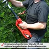 A person is using a red electric hedge trimmer against a backdrop of green bushes. Produktbild-Vorschau