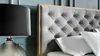 A close-up view of a tufted headboard and a bedside lamp. Náhled obrázku produktu
