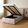 A bed with its storage compartment open, revealing the slatted base and storage space underneath. The bed is in a bedroom setting with curtains and a nightstand visible. Náhled obrázku produktu
