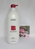 A large white bottle of Goldwell Elumen Color Shampoo with a red pump dispenser, positioned in front of a small photograph of a man wearing a hat and holding a piece of cake. Náhled obrázku produktu