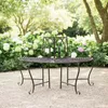 A metal garden bench with a decorative backrest is situated on a gravel path in a garden setting with blooming hydrangeas and trees. Náhled obrázku produktu