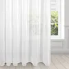 A white sheer curtain hangs in front of a window, with a view of greenery outside. Produktbild-Vorschau