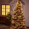 A Christmas tree decorated with warm white lights stands outside a house next to a window and a bench. Produktbild-Vorschau