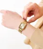 A person's hand adjusting a gold-colored watch on their wrist. Produktbild-Vorschau