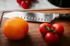 A close-up shot of a kitchen knife on a wooden cutting board with tomatoes. Voir les images du produit