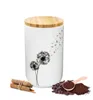 A white ceramic storage jar with a bamboo lid, decorated with a dandelion motif. Beside the jar are cinnamon sticks and coffee beans with ground coffee. Produktbild-Vorschau