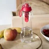 A water filter bottle with a red lid and filter, placed on a wooden surface next to an apple and bananas. A bowl of strawberries is visible in the background. Anteprima dell’immagine prodotto