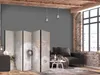 A room divider with a dandelion print is placed in a living room setting next to a sofa and a window. Produktbild-Vorschau