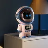 A pink astronaut-shaped smart speaker and alarm clock sits on a nightstand next to a lamp. Produktbild-Vorschau