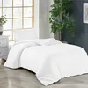 A white duvet cover and pillow are neatly arranged on a bed in a room with a large window and a potted plant. Produktbild-Vorschau