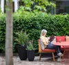 A woman sits on a bench in a garden, reading a book. Produktbild-Vorschau