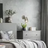 A bedroom scene with a bed, dresser, and wall lamp. Produktbild-Vorschau