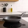 A frying pan sits on a modern induction stovetop in a kitchen setting. Produktbild-Vorschau