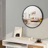 A round black mirror hangs on a light gray wall above a white console table. The mirror reflects a living room scene with sofas, chairs, and artwork. On the table are a framed picture, a box, and a glass mug. Produktbild-Vorschau