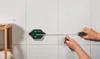 A person is using a laser level and tape measure on a tiled wall. Produktbild-Vorschau