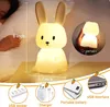 A glowing bunny night light is shown on a table next to a sleeping person. Several inset images show the light's features and accessories. Produktbild-Vorschau