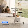 A white fitness bike with a table attachment is placed on a wooden floor, with a woven chair and potted plants in the background, suggesting a home or home office setting. Voir les images du produit