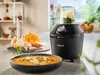 A black Philips blender sits on a kitchen counter, next to a bowl of soup and some ingredients. The blender has a glass container with food inside. Anteprima dell’immagine prodotto