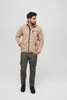 A man is standing and posing in a studio setting, wearing a beige fleece jacket and gray cargo pants. Anteprima dell’immagine prodotto