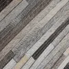 A close-up view of a rug made of stitched strips of cowhide in various shades of gray, brown, and beige. Voir les images du produit