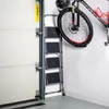A stepladder is placed next to a garage door, with a bicycle hanging on the wall above it. Náhľad obrázku produktu
