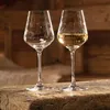 Two wine glasses, one empty and one filled with white wine, are placed on a wooden surface. Náhľad obrázku produktu