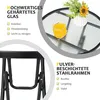 A close-up of a small round table with a glass top and metal frame, featuring a glass of orange juice and a small plant. Produktbild-Vorschau