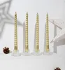 Four gold spiral candles in clear holders on a white surface with a pinecone and a star decoration in the background. Anteprima dell’immagine prodotto