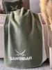 A green blanket with white text and a logo is draped over a sofa, with a pillow in the background. Produktbild-Vorschau
