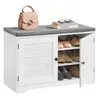 A white shoe cabinet with a gray upholstered top, featuring two doors and open shelving. A pink handbag and two books are placed on top of the cabinet. Produktbild-Vorschau