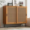 A wooden sideboard with cane-woven sliding doors, standing on dark metal legs, with decorative items on top. Produktbild-Vorschau