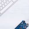 A white keyboard and a blue electronic board are placed on a white wooden surface. Anteprima dell’immagine prodotto