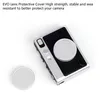 A close-up shot of a camera lens protective cover and a separate lens cap, both silver, against a white background. The camera body is partially visible, with black textured grip and silver accents. Produktbild-Vorschau