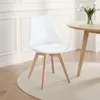 A white dining chair with wooden legs is placed on a light-colored rug in front of a white paneled wall. Produktbild-Vorschau