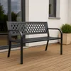 A black metal garden bench sits on a wooden deck in front of a modern building. Anteprima dell’immagine prodotto