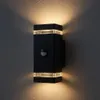 A black outdoor wall light with a motion sensor mounted on a textured gray wall. Produktbild-Vorschau