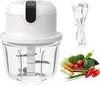 A white electric vegetable chopper with a clear glass bowl, a USB charging cable, and a selection of fresh vegetables. Produktbild-Vorschau
