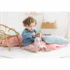 A young child is playing with a doll on the floor, feeding it with a bottle. Produktbild-Vorschau