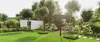 A beautifully landscaped garden featuring a modern pergola with a wooden bench underneath, surrounded by lush greenery and white hydrangeas. Produktbild-Vorschau