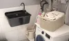 A laundry room scene with a sink, washing machine, laundry basket, and cleaning supplies. Produktbild-Vorschau