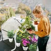 A woman is tending to plants in a mini greenhouse on a balcony. Voir les images du produit