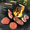 A fire pit with meat and grilling tools on a flat surface. Produktbild-Vorschau