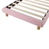 Close-up view of the corner of a pink upholstered bed frame with wooden legs and a wooden slatted base. Produktbild-Vorschau