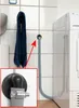 A close-up view of a washing machine drain hose connected to a wall fitting, with a towel hanging nearby. Podgląd zdjęcia produktu